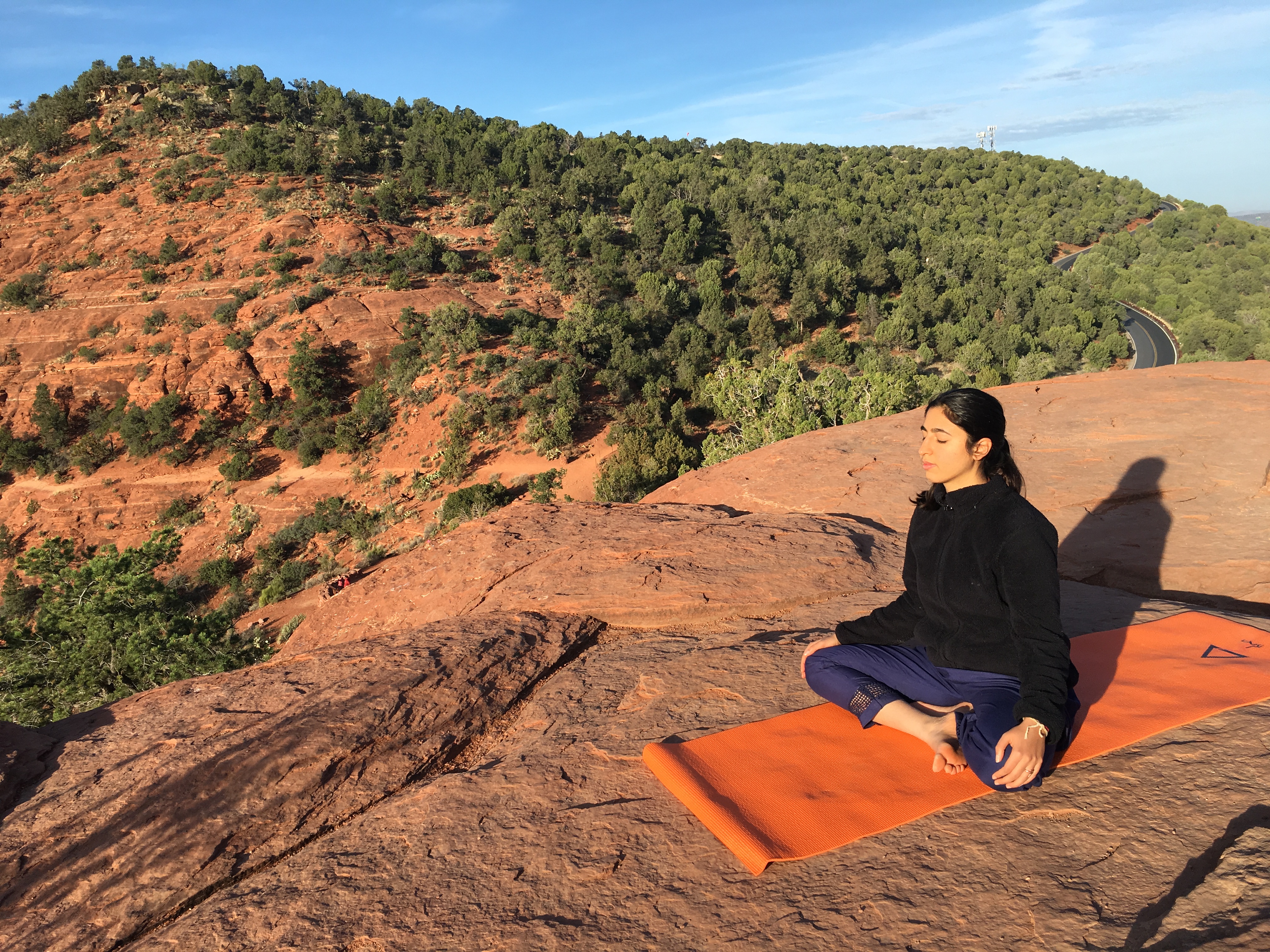Rasika Sethi sitting in meditation on red rock, a green hillside behind her.